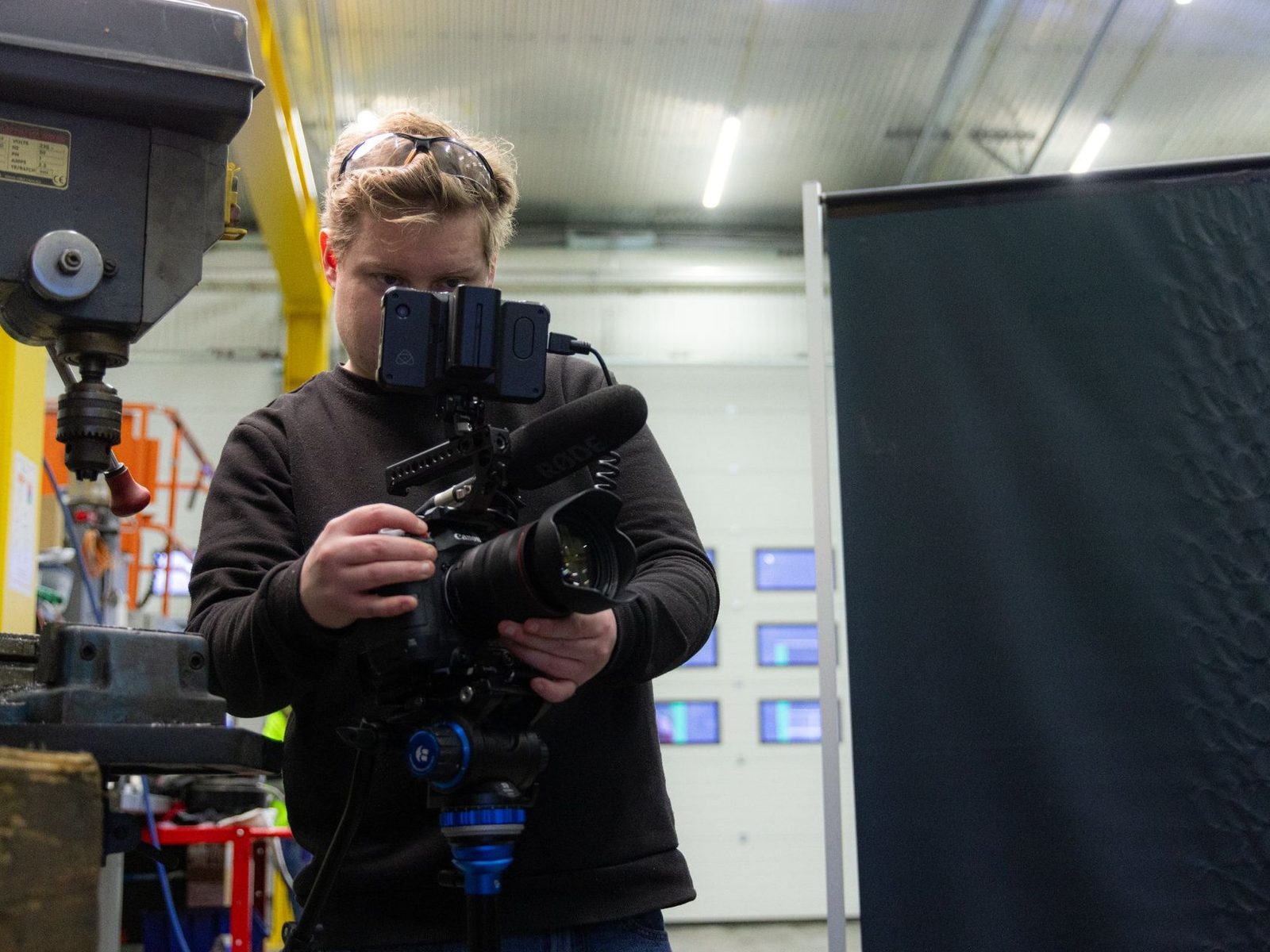 Fotograf filmer med videokamera på stativ i en industrihall med maskiner