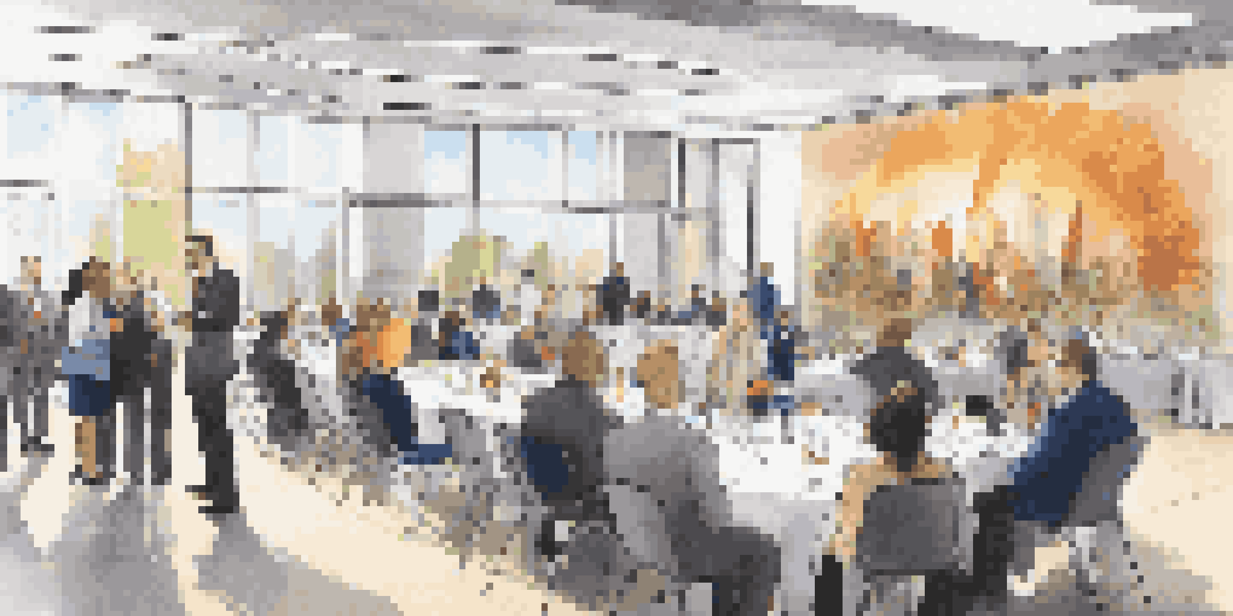 A lively scene of an alumni networking event in a bright conference hall, with groups of diverse people talking and banners in the background.