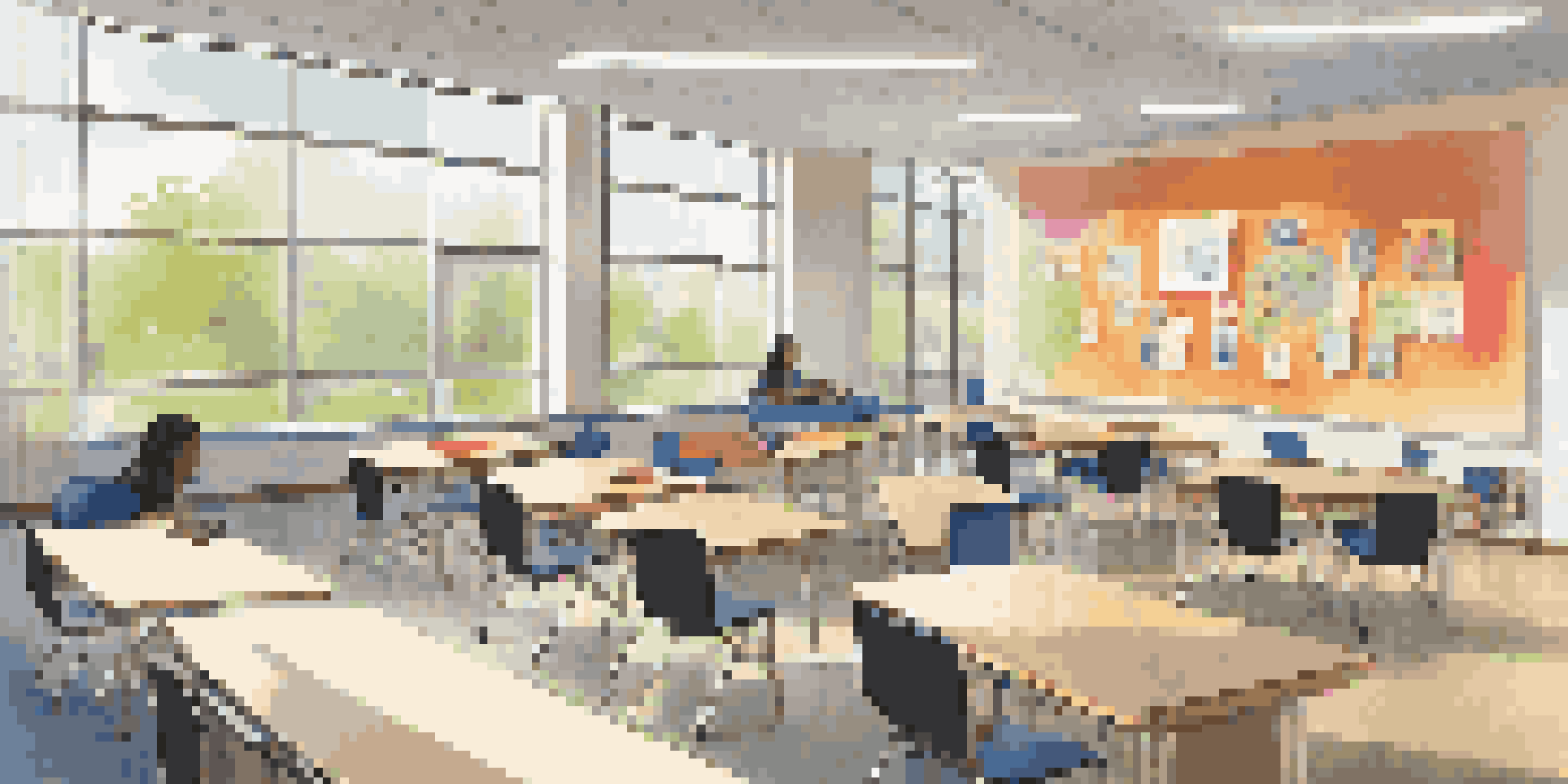 A bright, modern classroom with students sitting at circular tables, discussing in groups with natural light coming through the windows.
