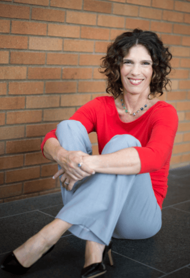 Meg Van Deusen seated beside a brick wall.