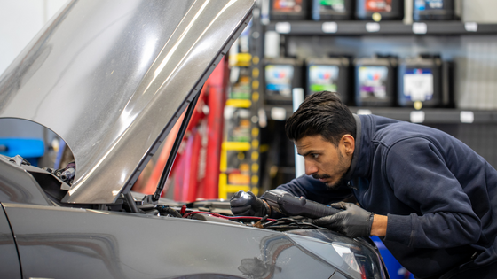 mechanic shining light under hood of silver car