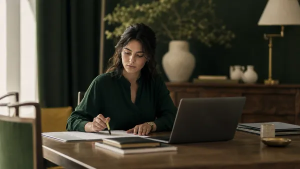 Docente in una sala insegnanti con calendario cartaceo e laptop aperto, evidenziatore e documenti ordinati sul tavolo; atmos…