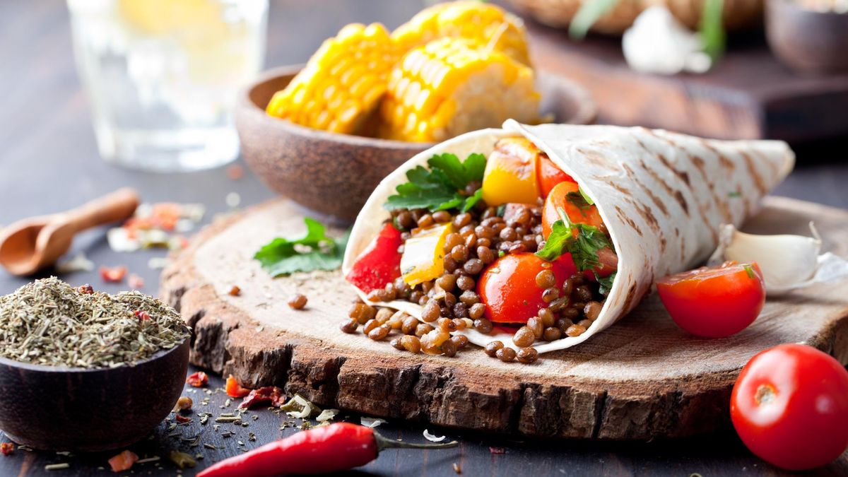 Vegan tortilla wrap, roll with grilled vegetabes and lentil and boiled corn cob on a wooden background