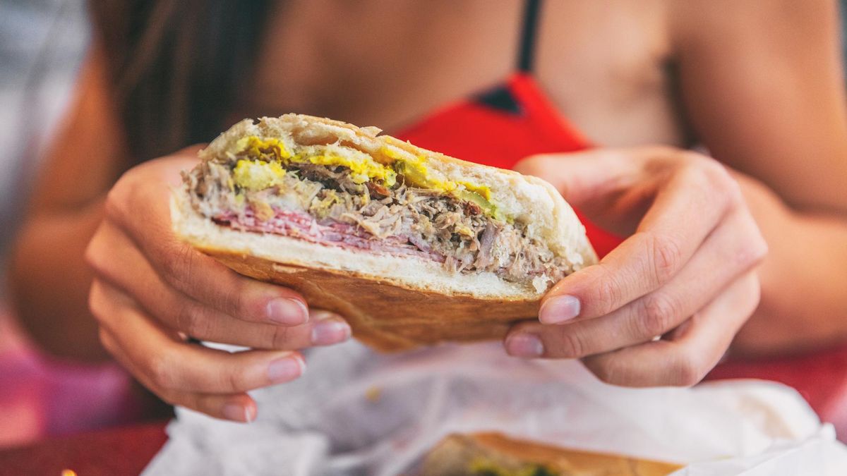 Cuban sandwich closeup woman holding local food at typical cafe outside. Pressed cuban bread with roasted pork, salami sausage, swiss cheese, mustard, typical cuba dish.