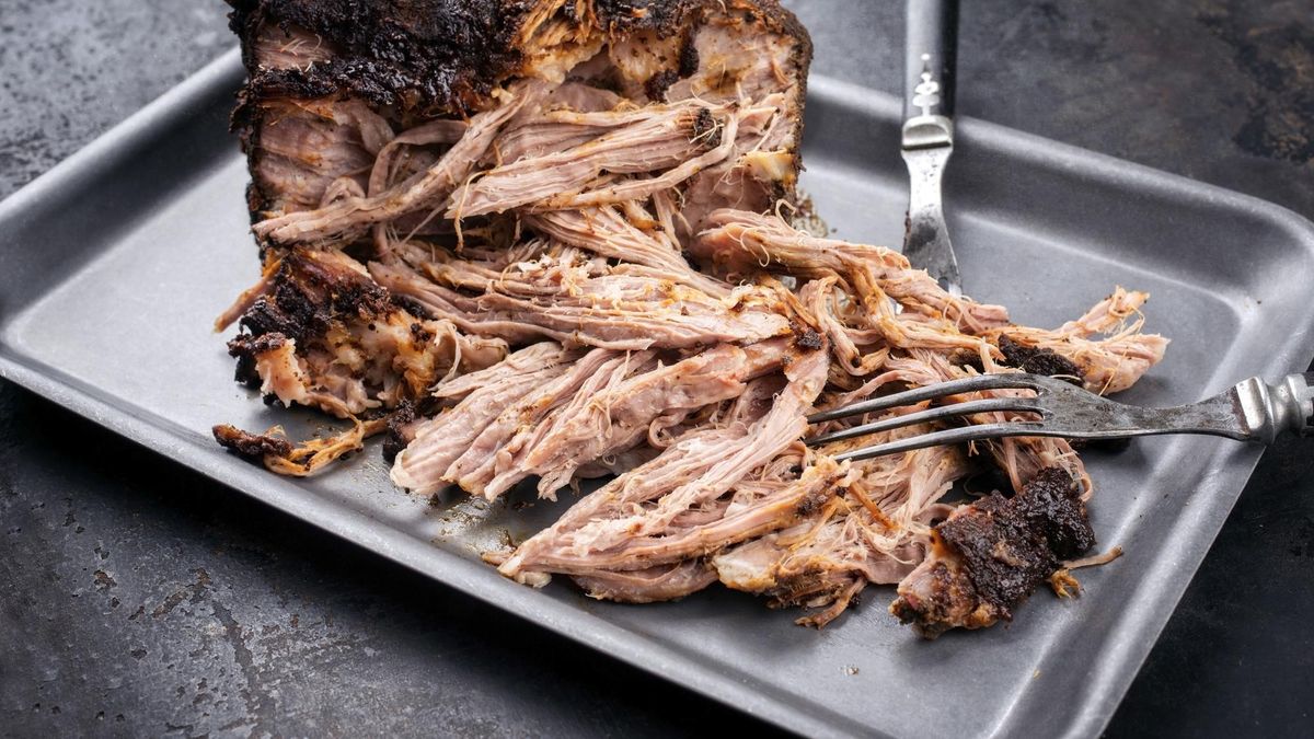 Traditional barbecue pulled pork piece of Bosten butt torn to bits as close-up on a board