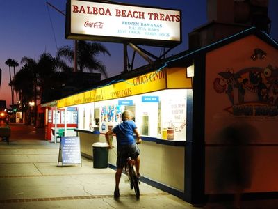 A teenage boy bikes up to an ice cream stand in Newport Beach California at dusk