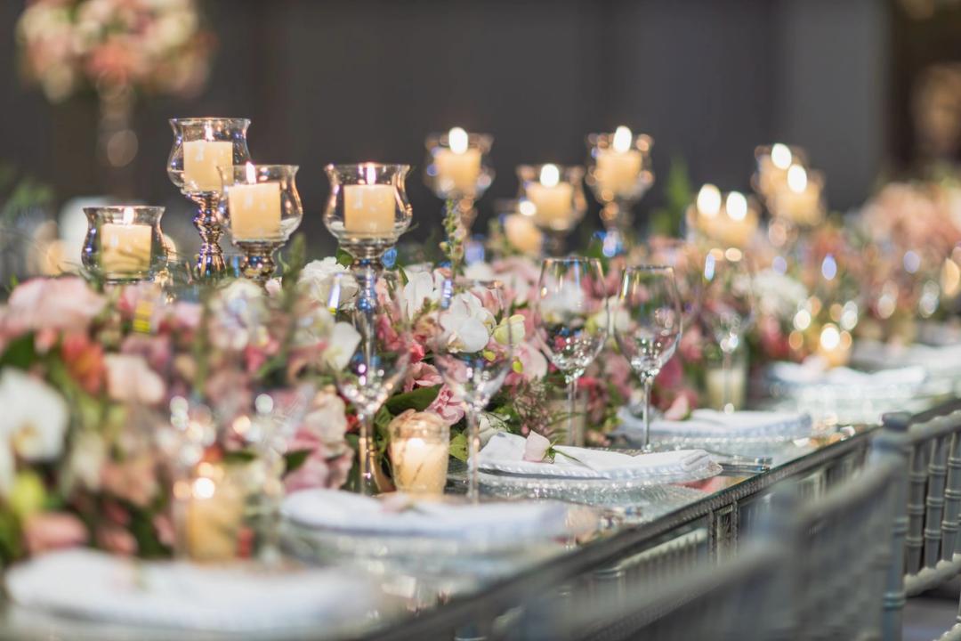 A long wedding table set with candles in glass holders, flowers, wine glasses and folded napkins.