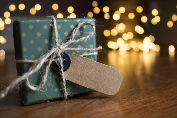 Un petit cadeau emballé dans du papier vert à losanges dorés, noué de ficelle avec une étiquette kraft vierge, sur une table en bois devant des lumières chaudes floues.