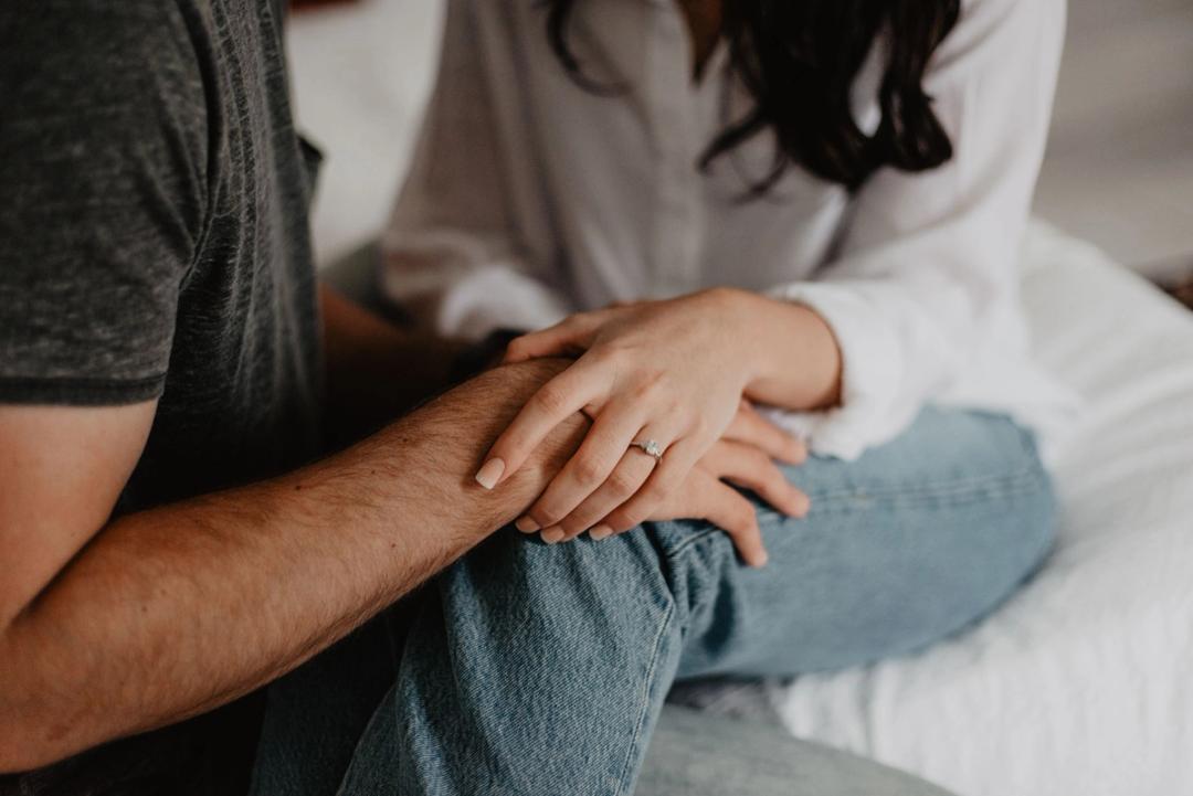 Une femme qui porte une bague de fiançailles pose la main sur le bras d'un homme, assis tout près d'elle.