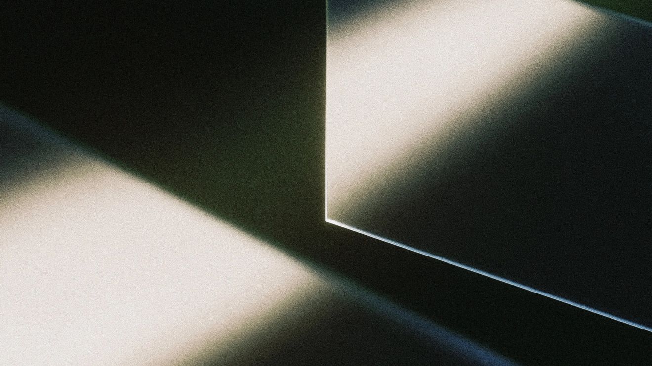 Abstract glass panel with illuminated edges separating light and shadow against a dark background.