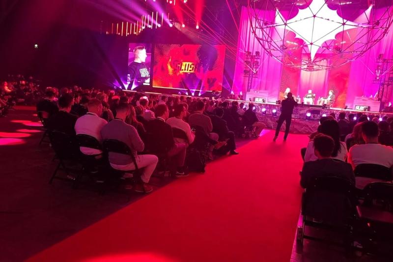 The Founder Stage at Slush 2025 in red and purple light, with people speaking on stage and a seated audience listening.