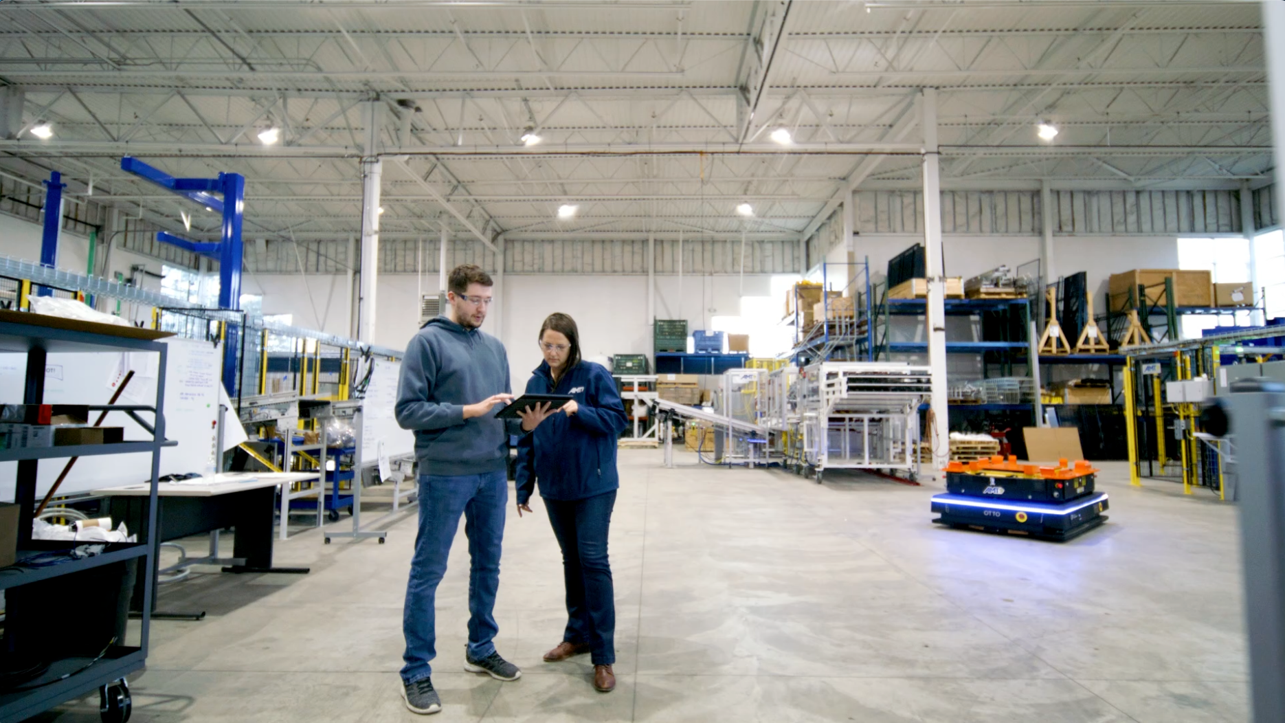 Partner representative on factory floor with customer, looking at a tablet while OTTO drives nearby