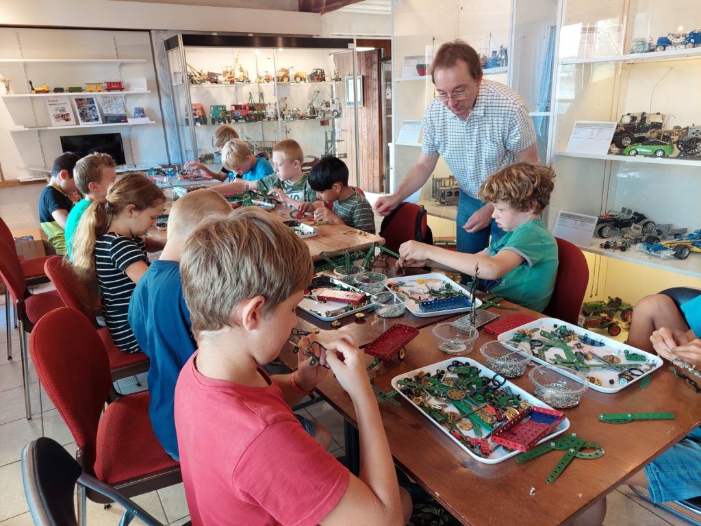 Kinder am Werktisch, ein Leiter hilft beim Zusammenbauen