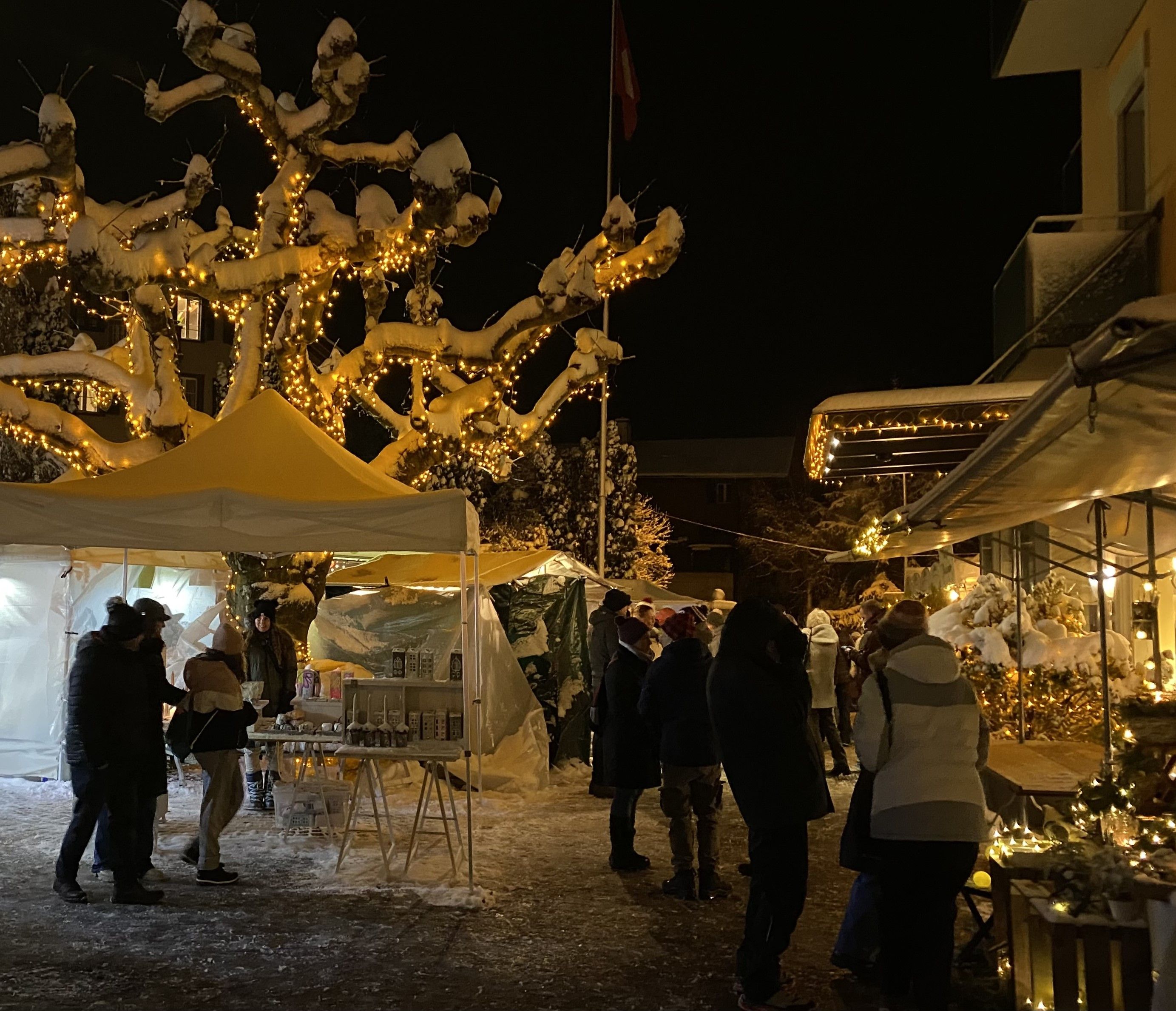 Der Weihnachtsmarkt bei Nacht mit beleuchteten Ständen und einem Lichterbaum