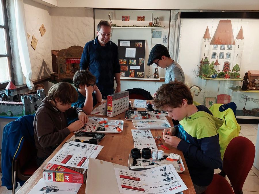 Kinder am Tisch, vor ihnen Bauanleitungen und Schalen mit Kleinteilen