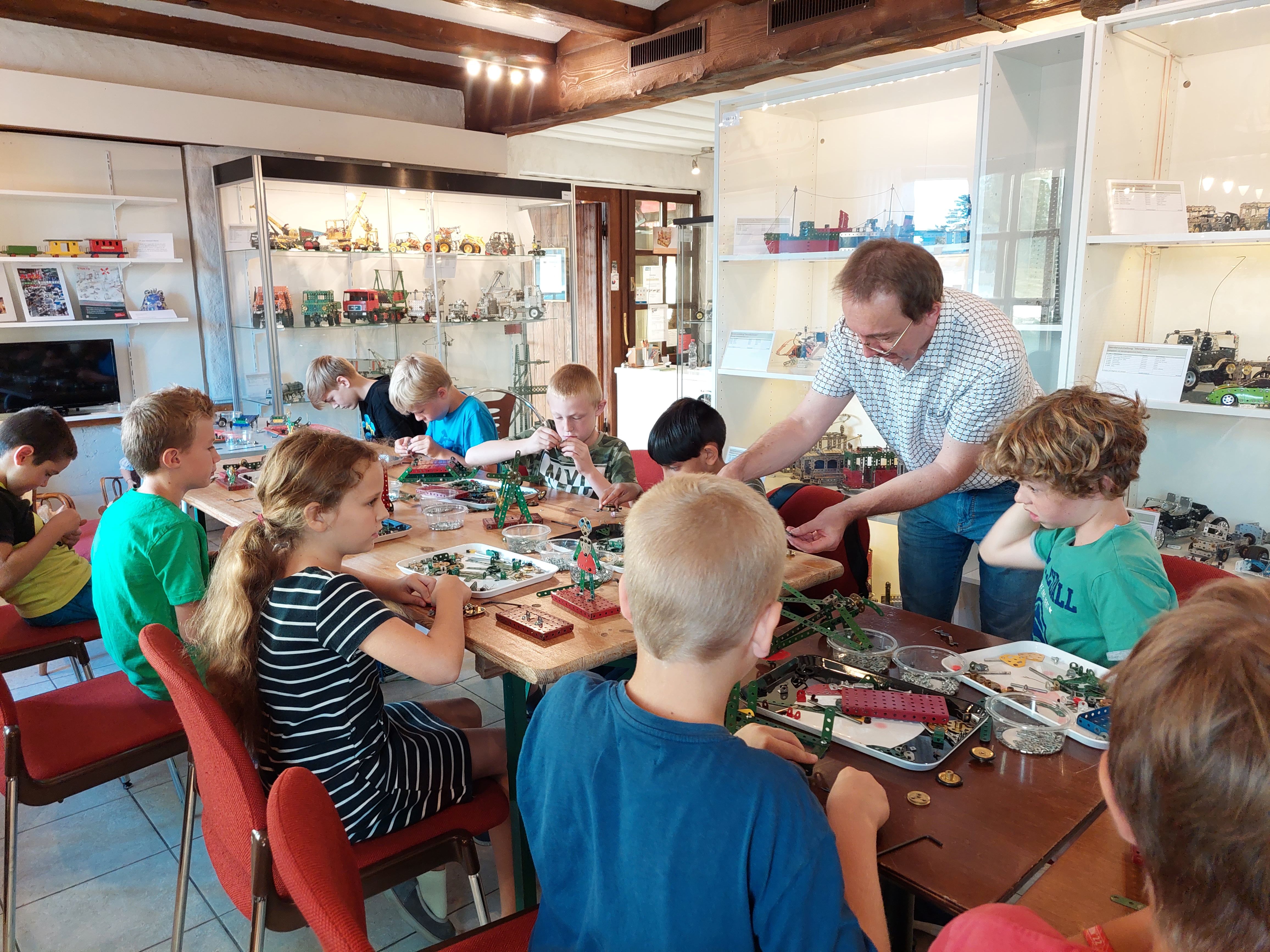 Kinder bauen an einem langen Tisch mit Metallbaukasten, im Hintergrund die Vitrinen des Museums