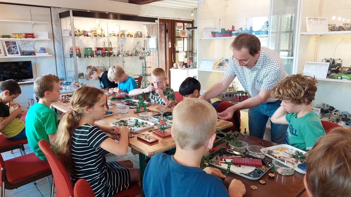 Kinder bauen an einem langen Tisch mit Metallbaukasten, im Hintergrund die Vitrinen des Museums