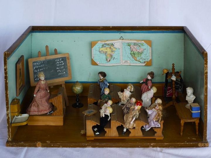 Diorama eines alten Schulzimmers mit Porzellanpuppen in Schulbänken, Wandtafel und Landkarte.