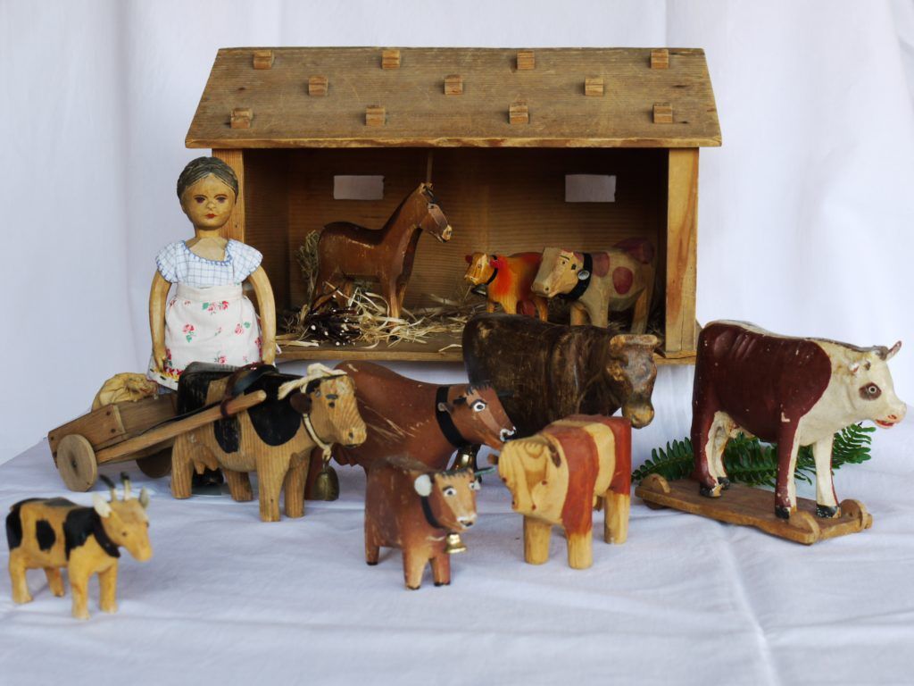 Hölzerner Spielzeugstall mit geschnitzten Kühen, Ziegen, einem Pferd und einer Bäuerinnenfigur.