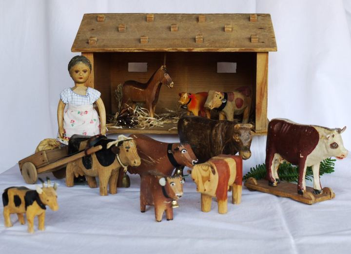 Hölzerner Spielzeugstall mit geschnitzten Kühen, Ziegen, einem Pferd und einer Bäuerinnenfigur.
