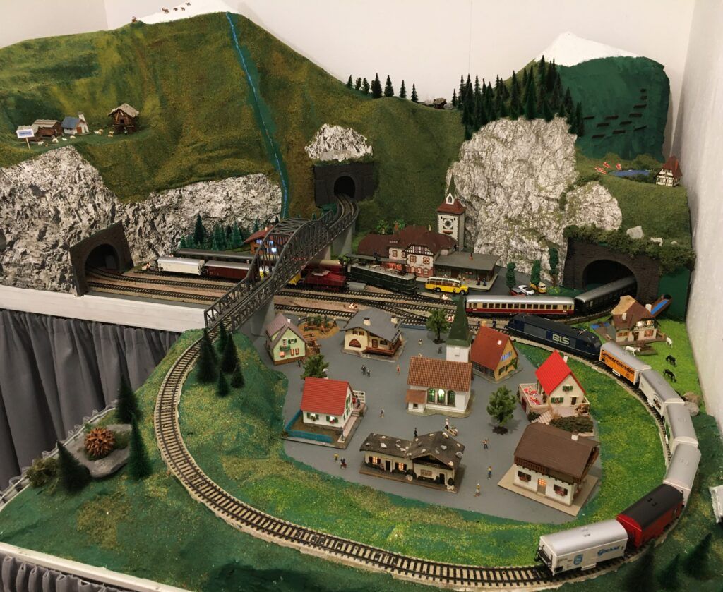 Modelleisenbahnanlage mit Bergen, Tunnels, einem Dorf und mehreren Zügen.