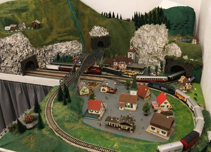 Modelleisenbahnanlage mit Bergen, Tunnels, einem Dorf und mehreren Zügen.
