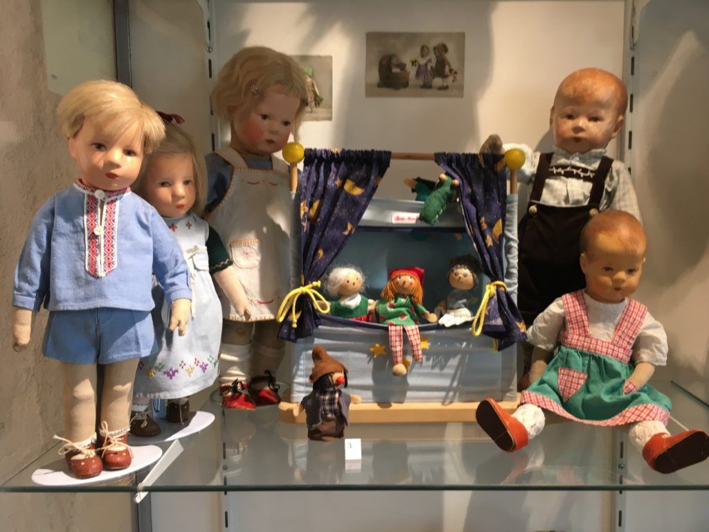 Vitrine mit Stoffpuppen in genähten Kleidern und einem kleinen Puppentheater.