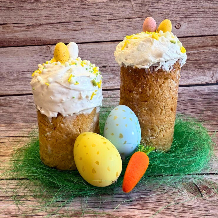 Two tall Paska Easter breads with white icing and pastel egg decorations