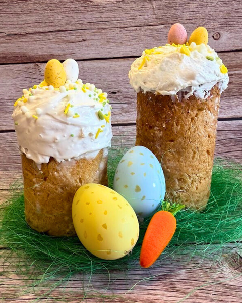 Easter Cake (Paska) by Olgish Cakes with white icing and mini eggs, traditional Ukrainian Easter sweet bread on a wooden background.