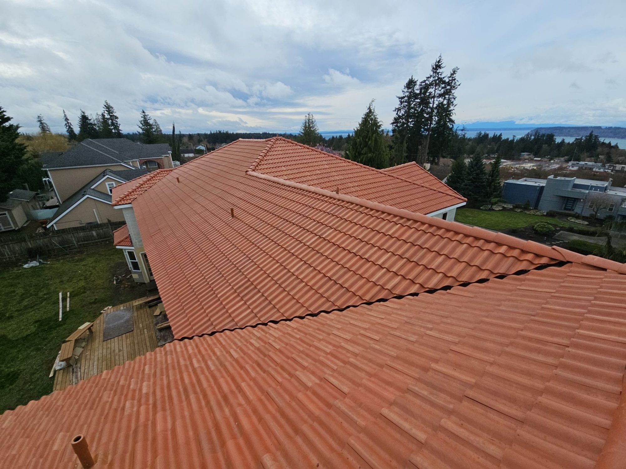 Ridge of the finished Antique Clay Brava composite Spanish barrel tile roof with the Sound and mountains beyond, Mukilteo, WA