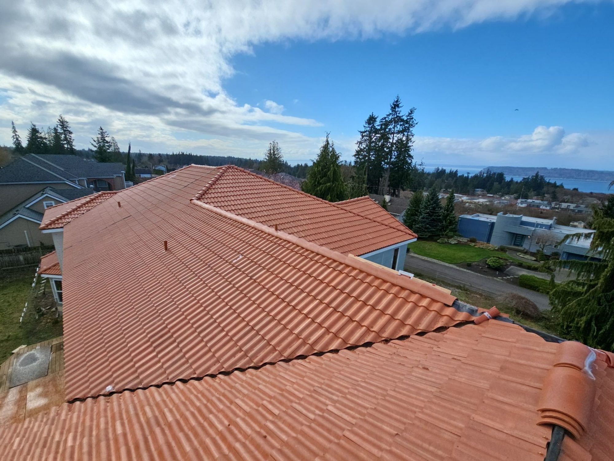Finished Antique Clay Brava composite Spanish barrel tile roof under blue sky looking out over Mukilteo toward Puget Sound, by Amor Roofing