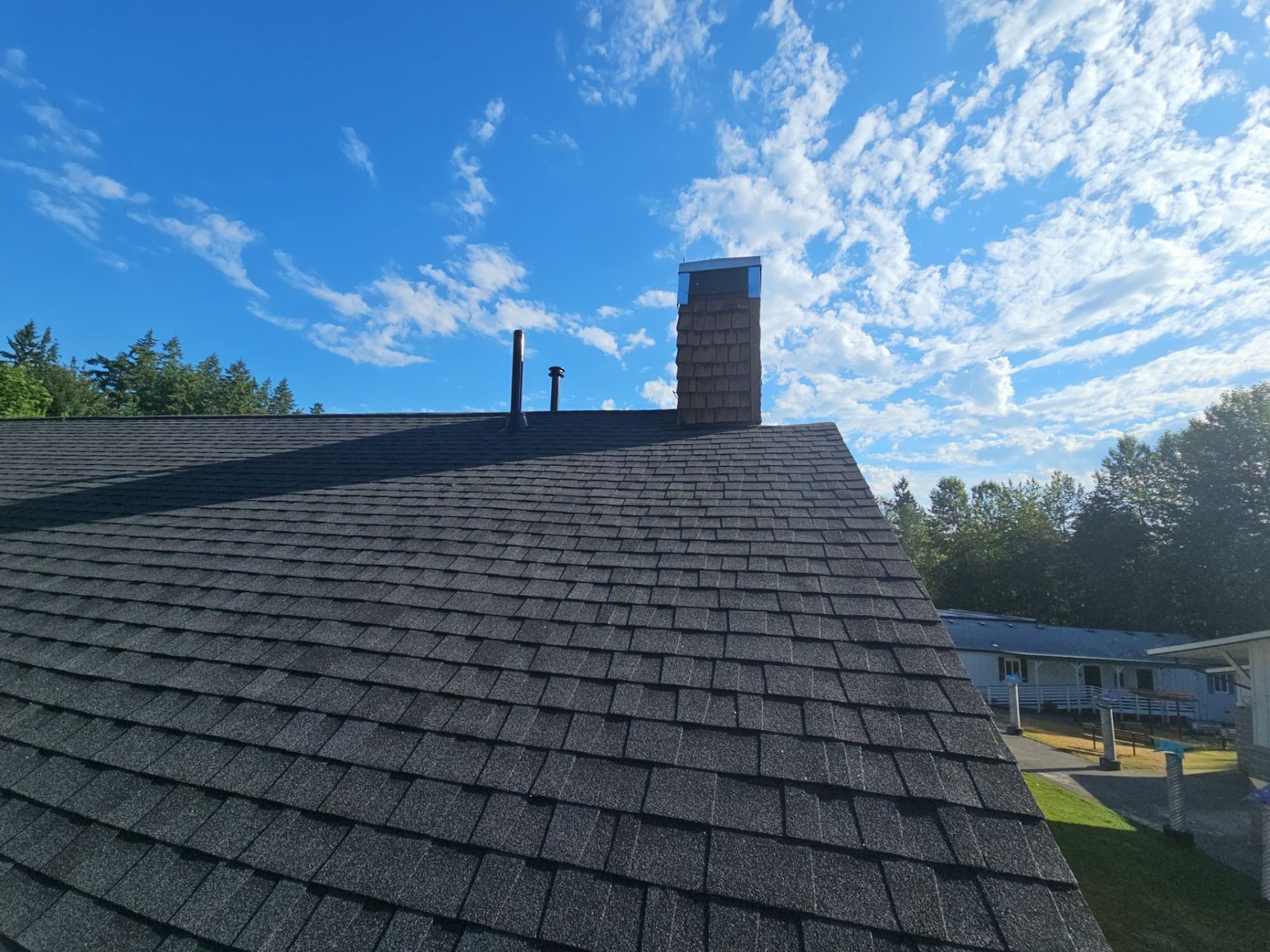 Cedar chimney and the finished Antique Black asphalt shingle roof under a dramatic sky, Woodinville, WA
