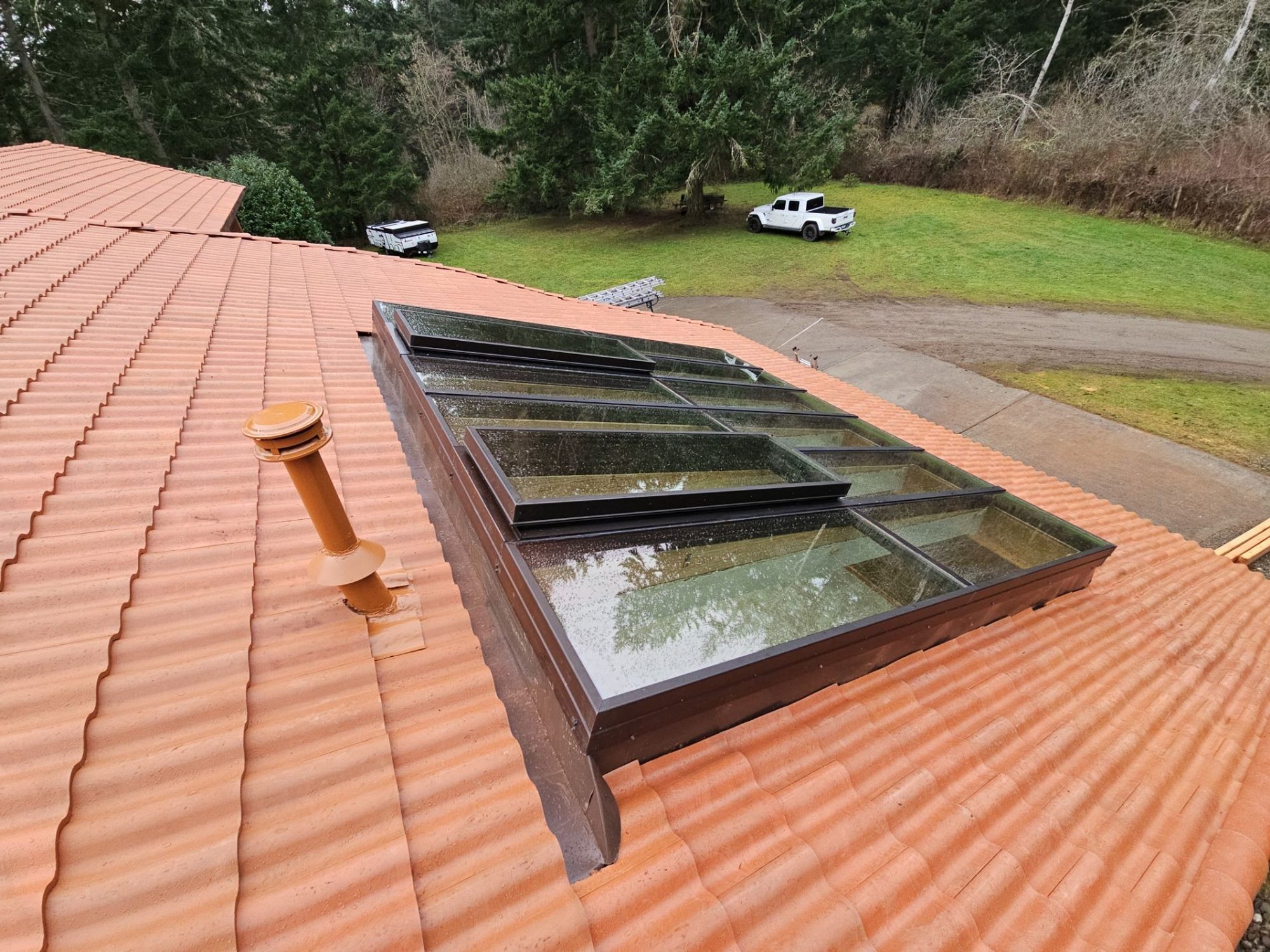 Skylight and pipe vent in the finished Antique Clay Brava composite Spanish barrel tile roof with the lawn beyond, Camano Island, WA