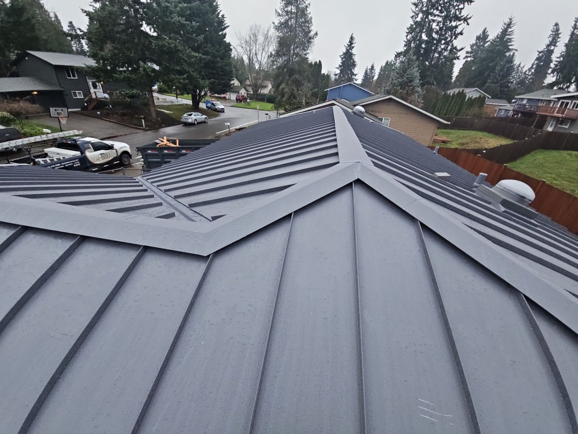 Hip and ridge seams of the finished Cascade Gray standing seam metal roof looking toward the neighborhood, Woodinville, WA