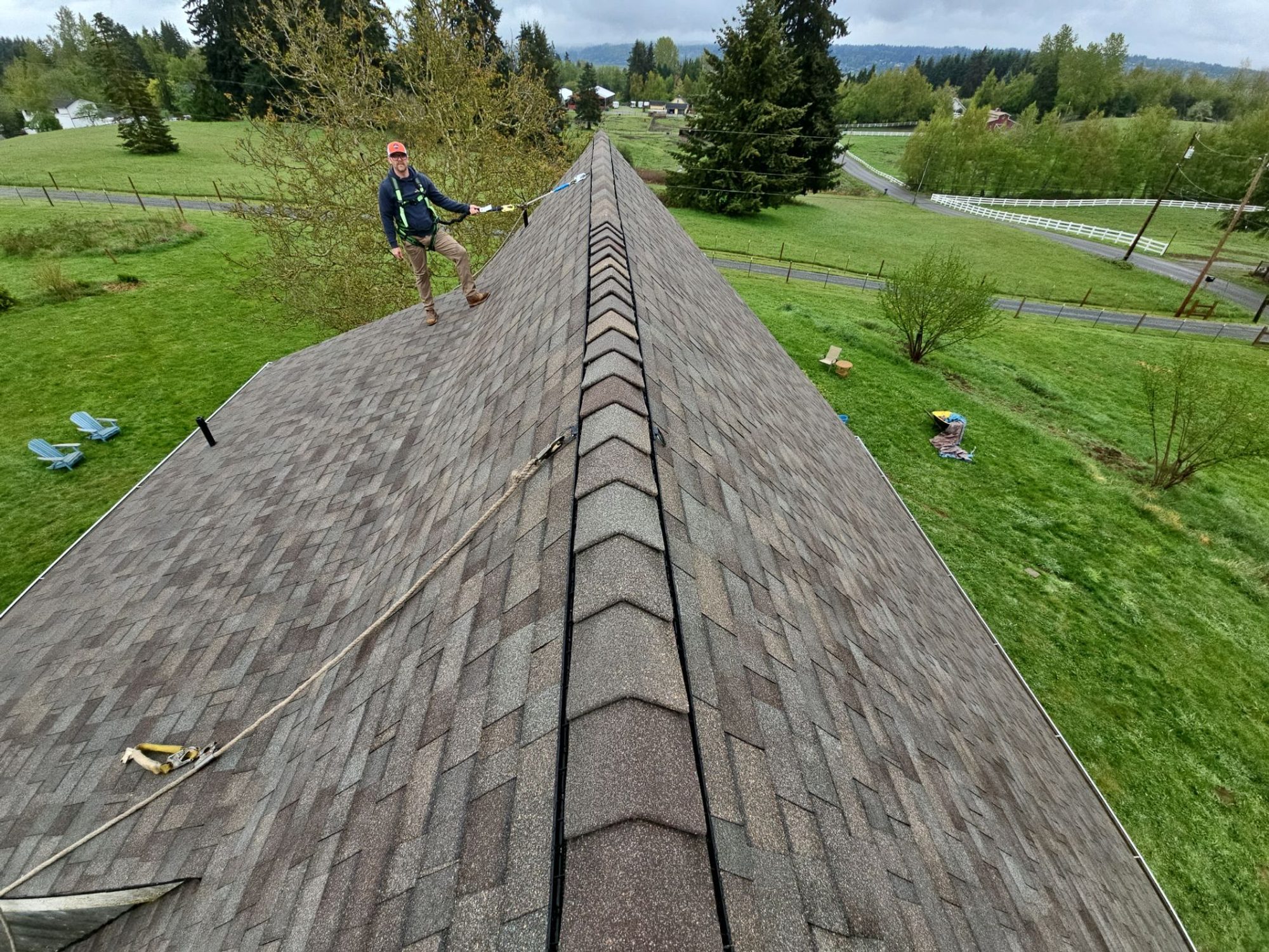 Amor Roofing crew member on the finished steep roof in Snohomish, new Malarkey Vista shingles in Natural Wood running down the ridge with green pastures beyond