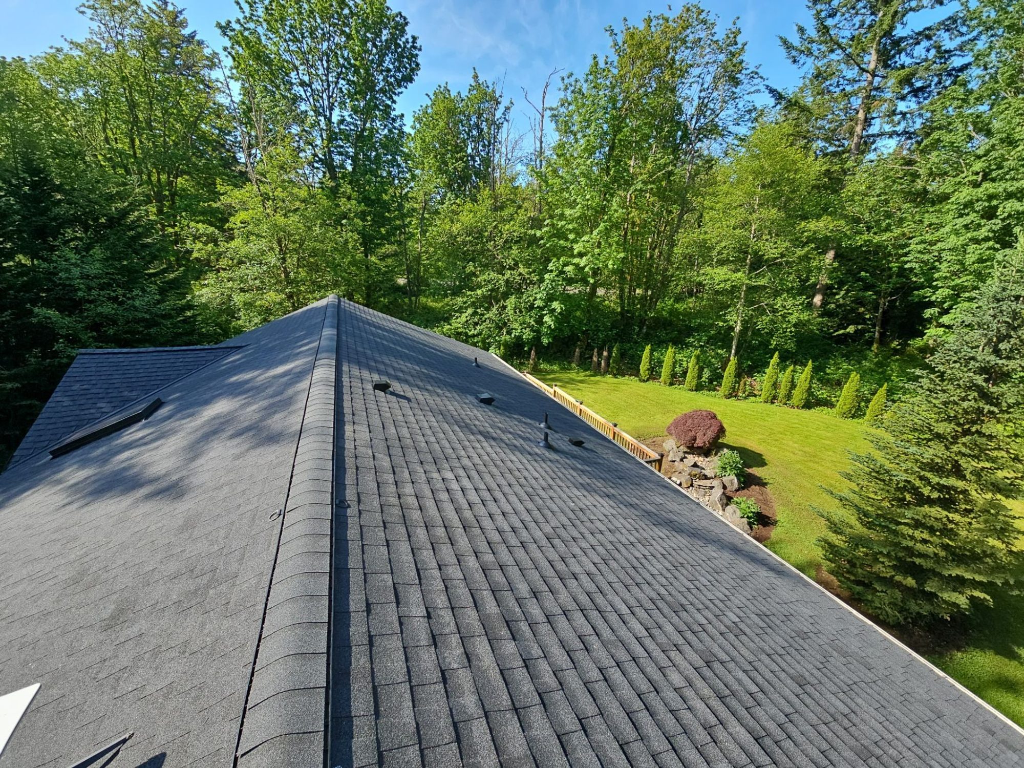 Hip peak of the Antique Black asphalt shingle roof with skylight under blue sky, Tulalip Bay, WA
