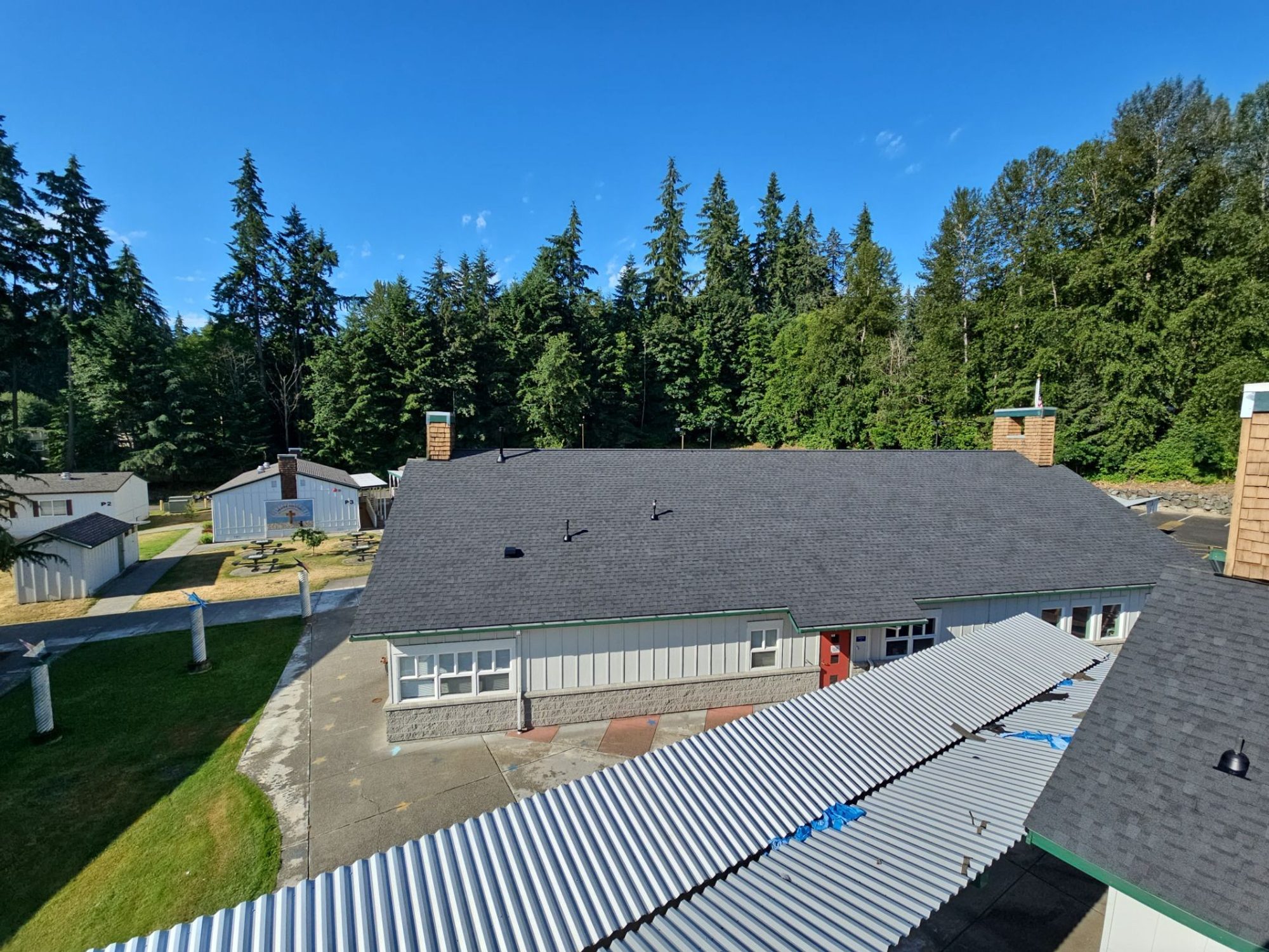 Evening view over the completed Antique Black asphalt shingle roof on the school's Building A with its cedar chimneys, Woodinville, WA, by Amor Roofing