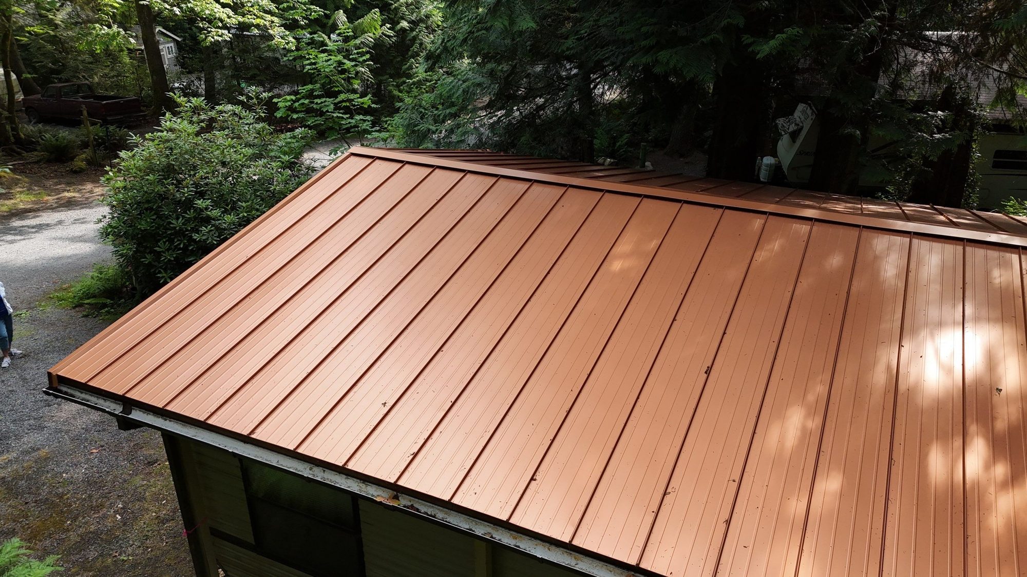 Drone view over the completed Copper Penny standing seam metal roof on a wooded Marysville, WA cabin, by Amor Roofing