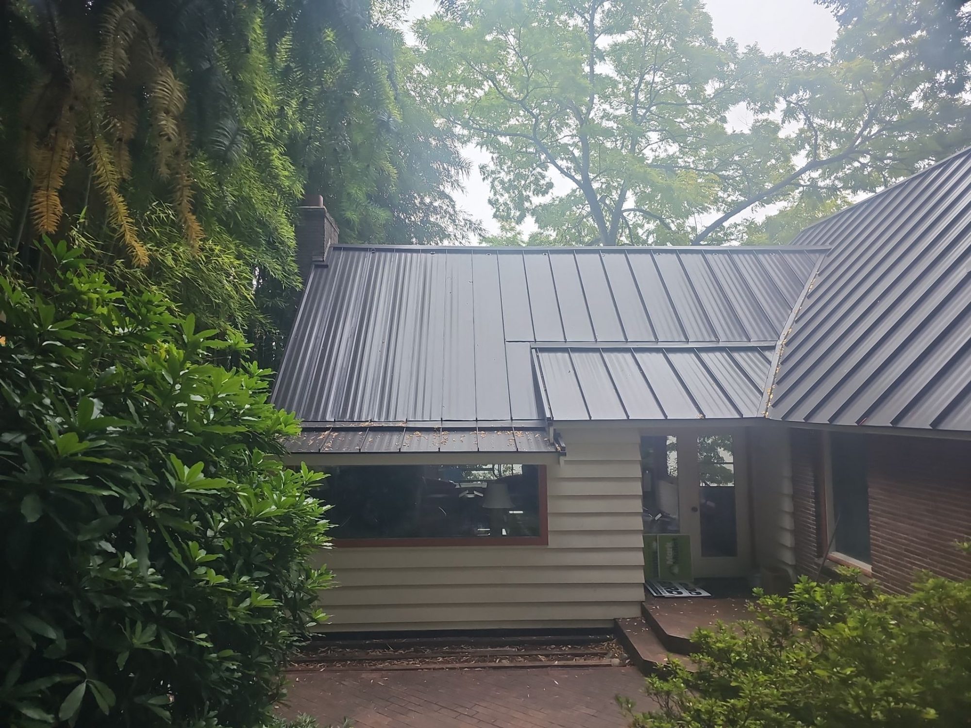 Front of a Bellevue, WA home with its finished Dark Bronze standing seam metal roof, brick and steep gable, by Amor Roofing
