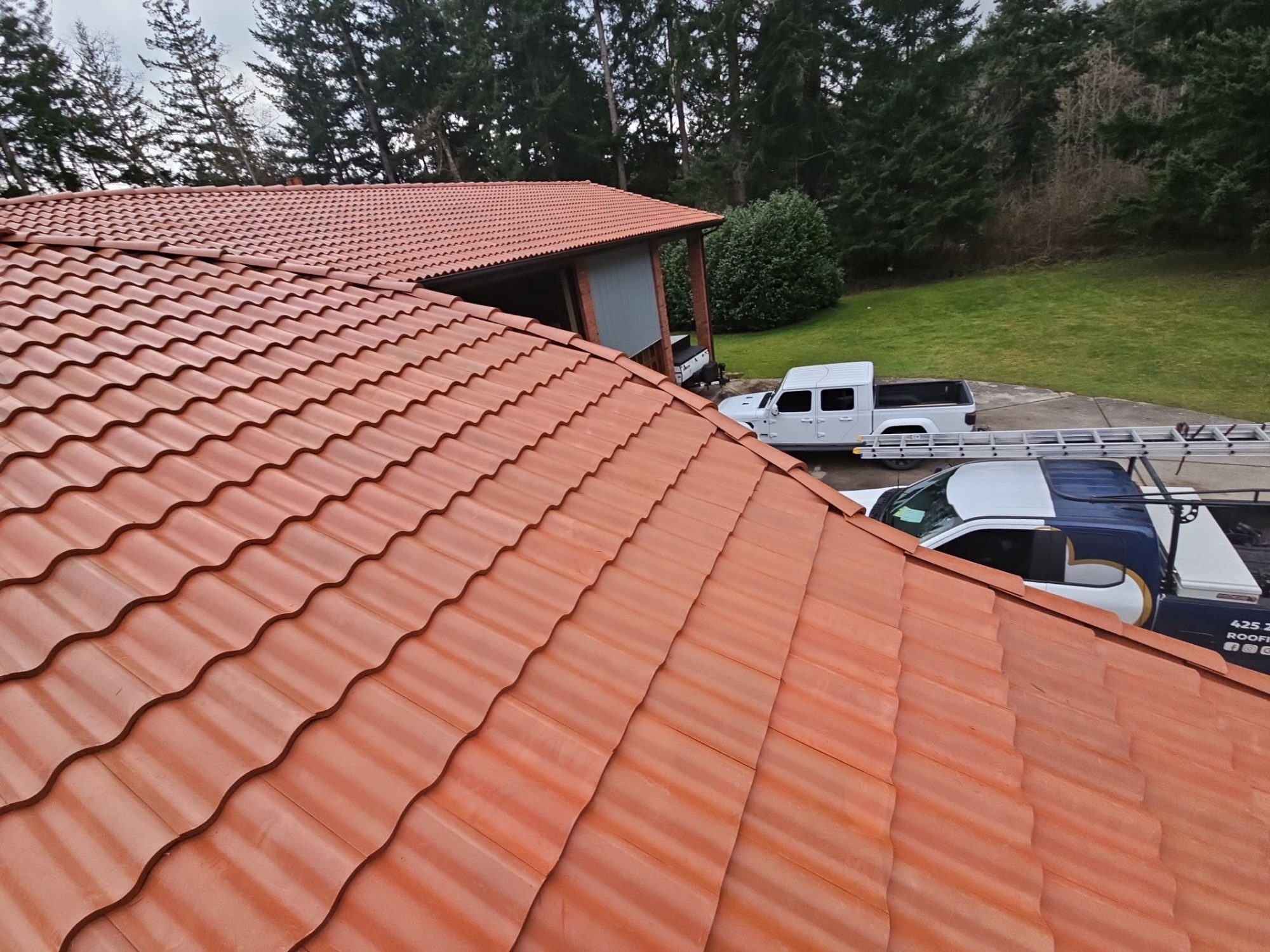 Finished Antique Clay Brava composite Spanish barrel tile roof from the ridge with Amor Roofing trucks below, Camano Island, WA