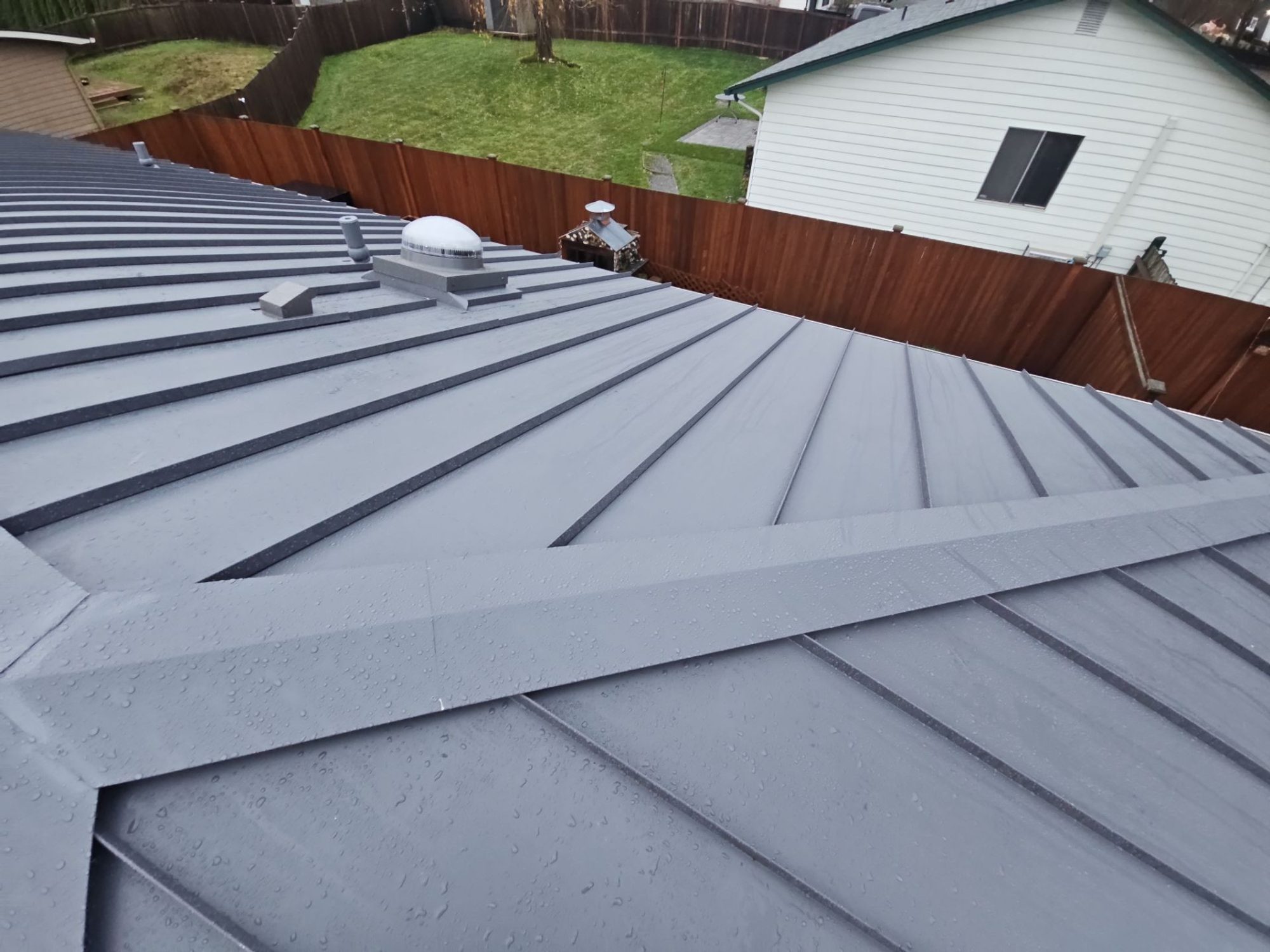 Ridge line of the Cascade Gray standing seam metal roof with the fence and neighboring homes, Woodinville, WA