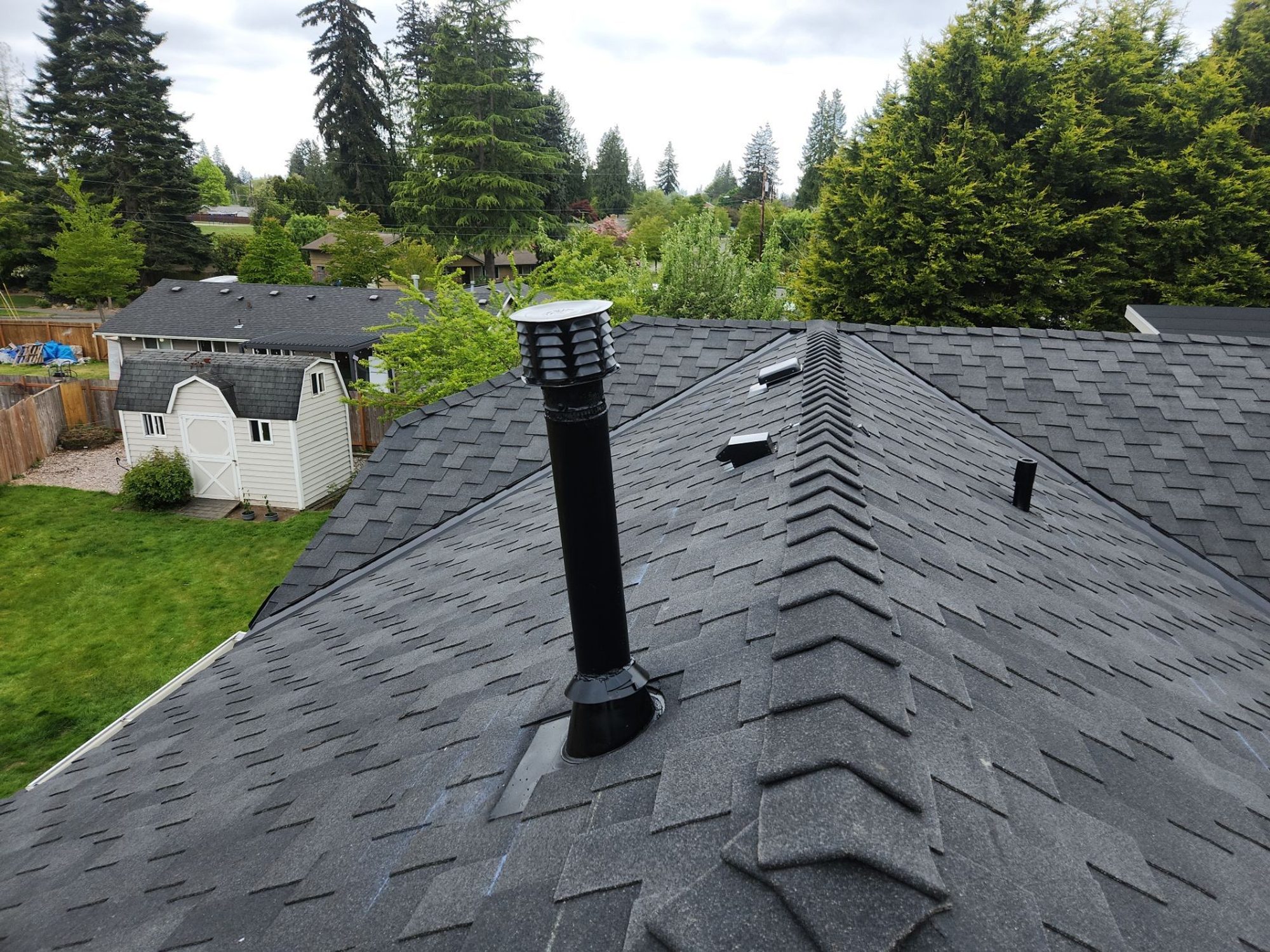 Ridge and pipe vent on the finished Midnight Black designer shake roof with the tree line behind, Brier, WA