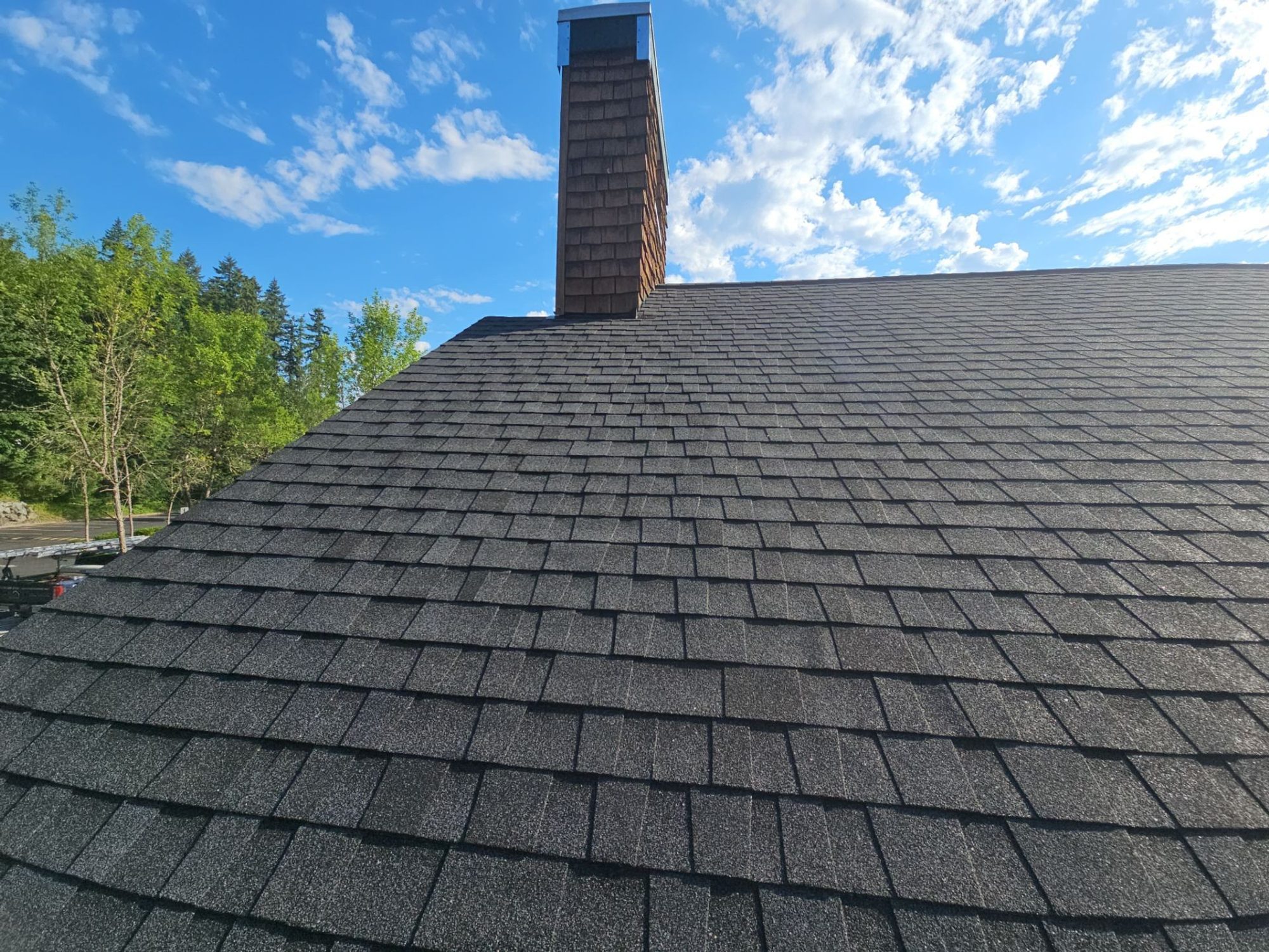Cedar chimney against the clouds on the finished Antique Black asphalt shingle roof, Woodinville, WA