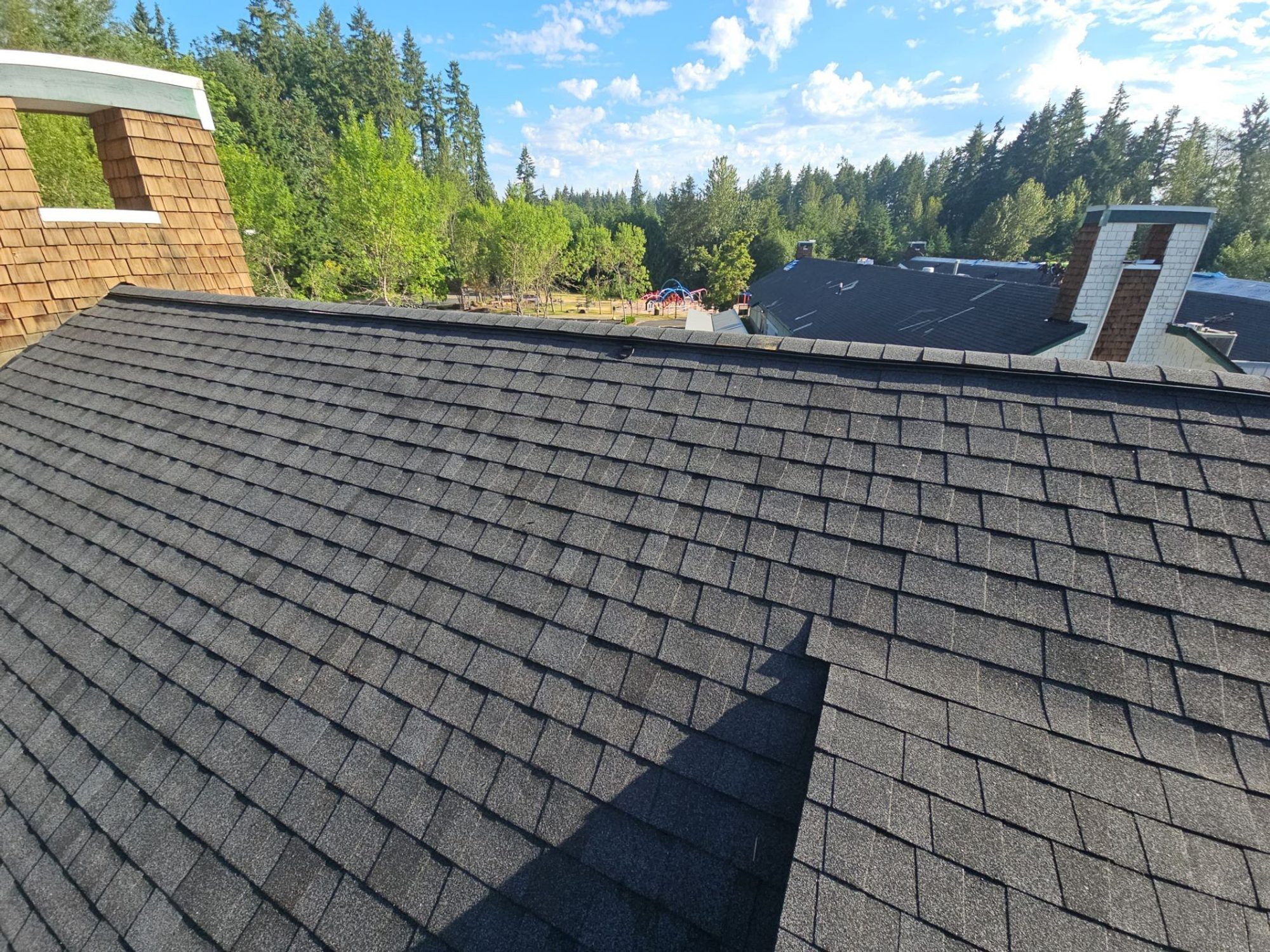 Twin cedar chimneys along the finished Antique Black asphalt shingle roof ridge, Building A, Woodinville, WA