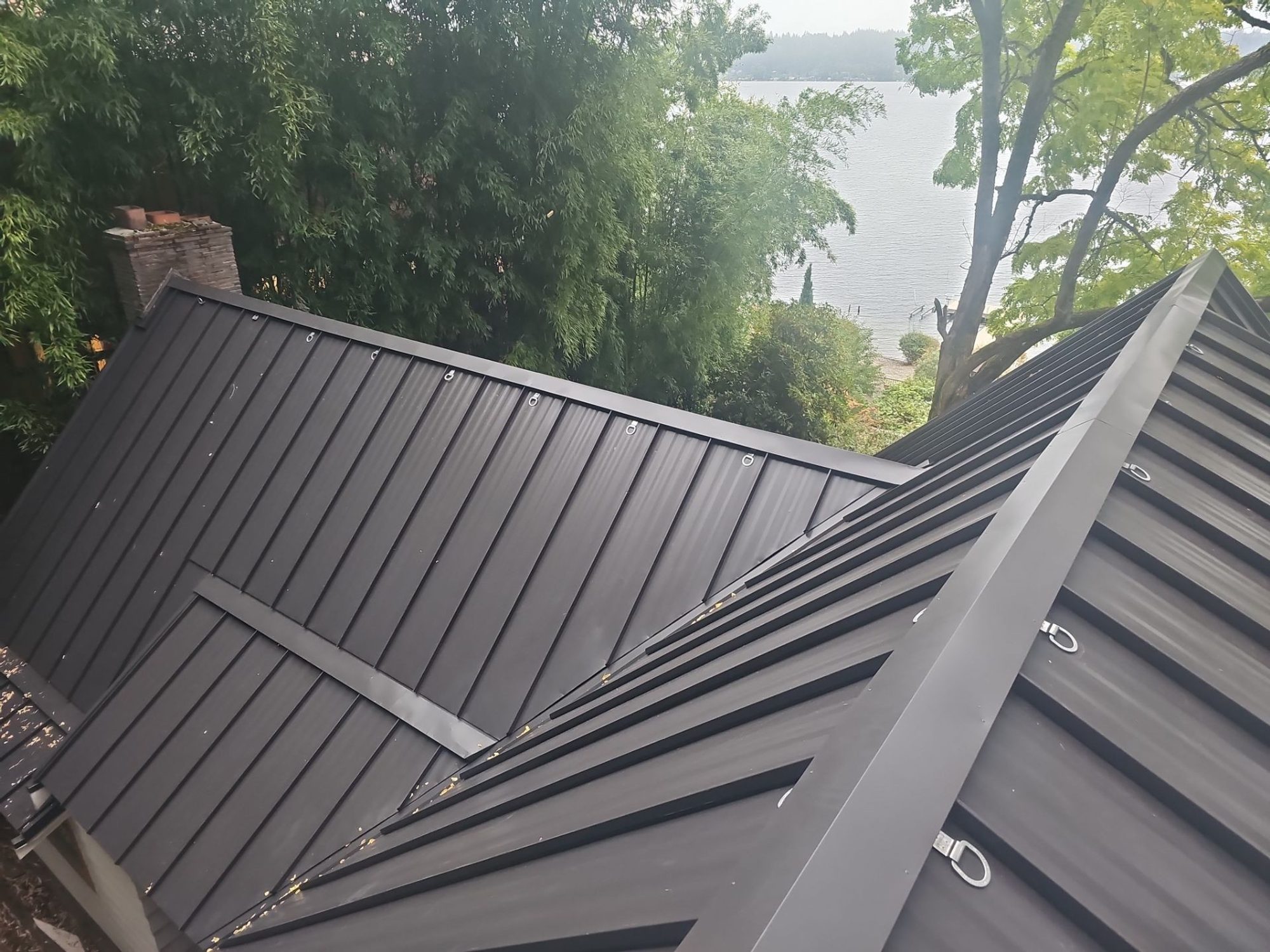 Hip peak and chimney on the finished Dark Bronze standing seam metal roof, Bellevue, WA