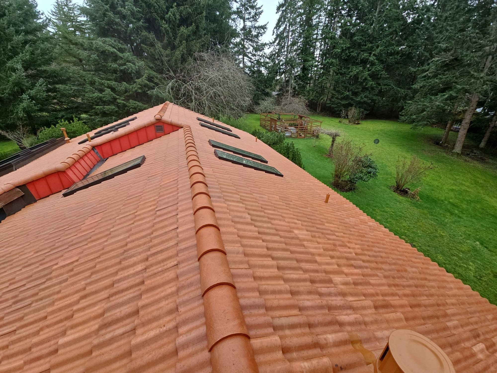 Ridge, skylights, and pipe vents on the finished Antique Clay Brava composite Spanish barrel tile roof above the lawn, Camano Island, WA