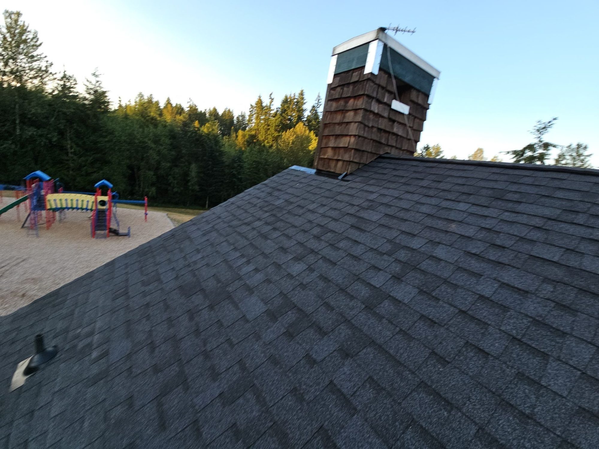 Building B's finished Antique Black asphalt shingle roof and chimney above the playground, Woodinville, WA