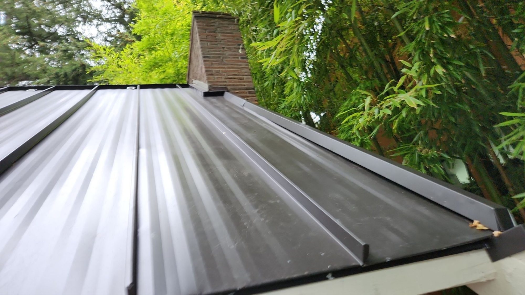 Standing seam panels of the Dark Bronze standing seam metal roof running to the brick chimney, Bellevue, WA