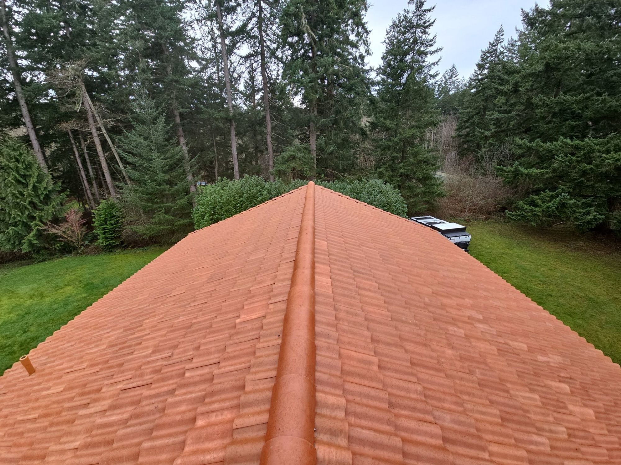 Long ridge of finished Antique Clay Brava composite Spanish barrel tile roof looking toward the trees, Camano Island, WA