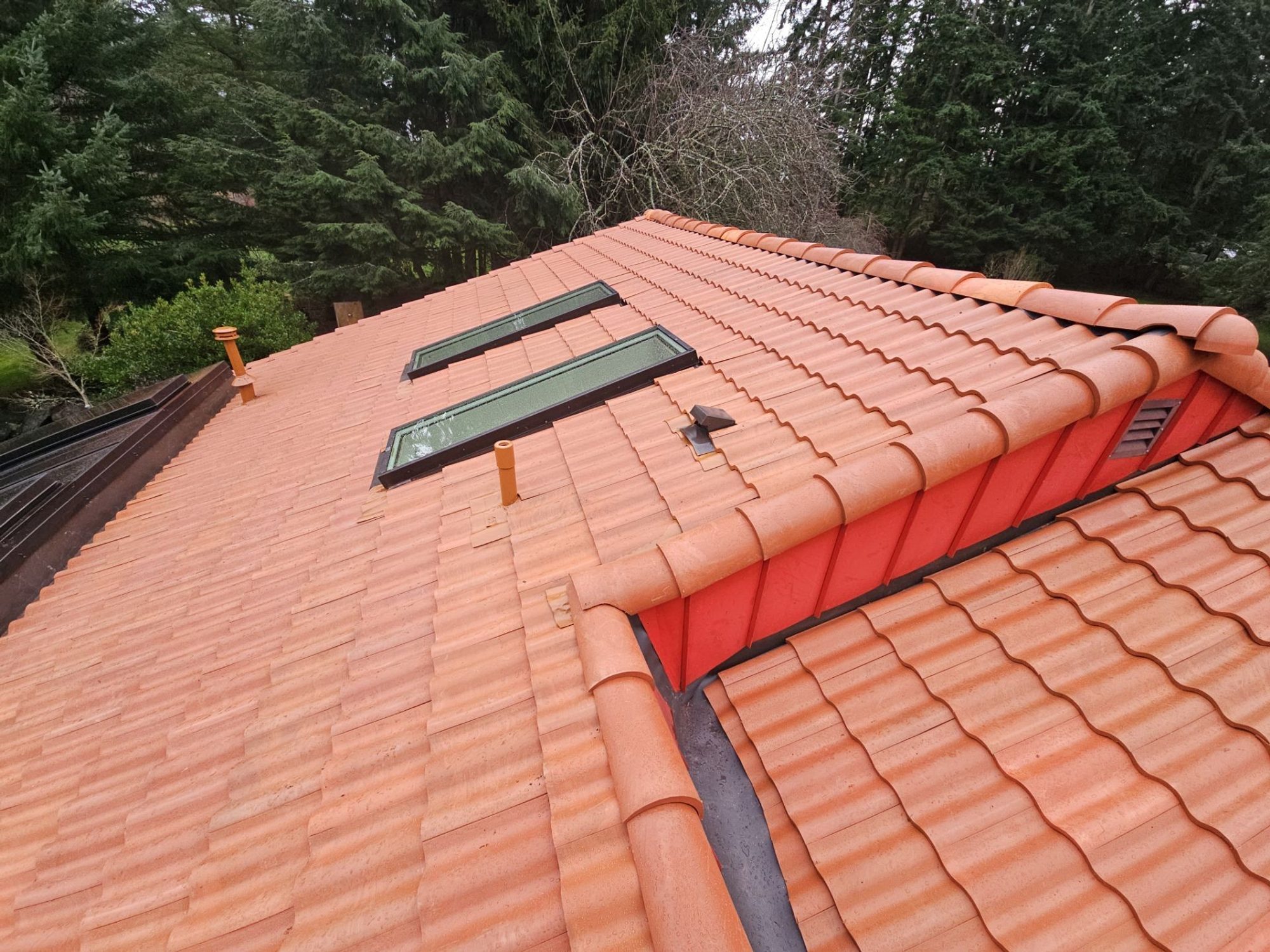 Roof step with red wall flashing and skylight in Antique Clay Brava composite Spanish barrel tile, Camano Island, WA